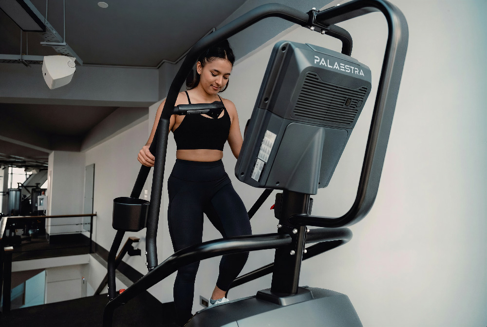 Ein Bild von einem Stepper im Fitnesstudio, worauf das Wortzeichen des Unternehmens drauf ist. IMG by: https://unsplash.com/de/fotos/eine-frau-auf-einem-laufband-in-einem-fitnessstudio-RzI-idjc8RQ