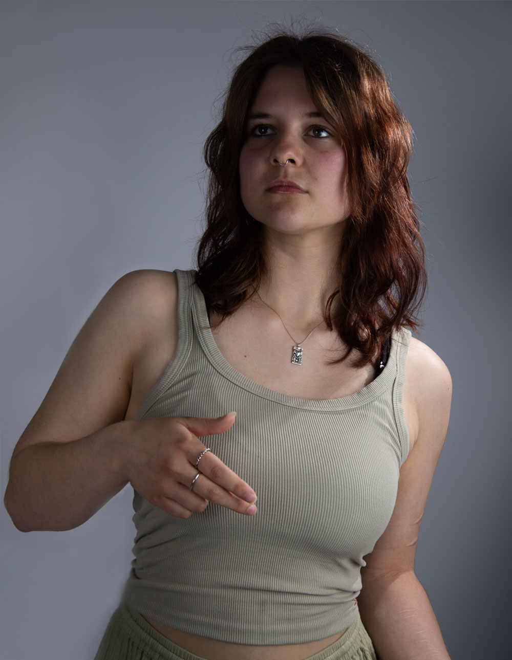 Verdania-Original_WebOpt Eine junge Dame mit roten Haaren und einem grünen Tanktop. Sie schaut zur Seite und hält ihre rechte Hand vor die Brust.